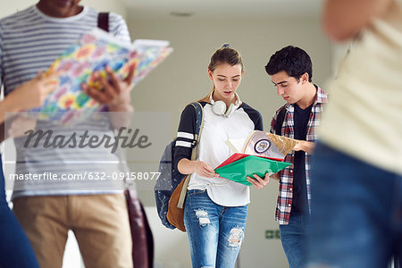 Classmates looking at textbook together in corridor