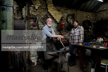 Senior blacksmith and son in blacksmiths shop, portrait