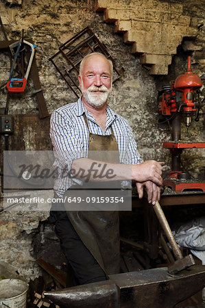 Blacksmith with hammer and anvil in blacksmiths shop, portrait