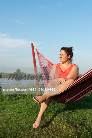 Woman relaxing in hammock by river, Broek, Friesland, Netherlands