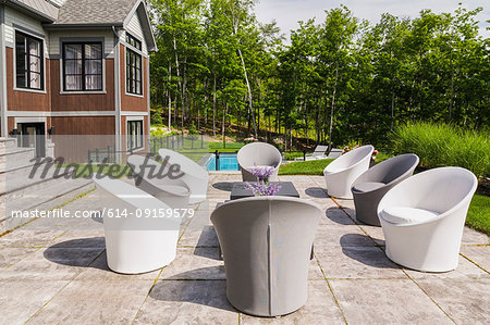 Chairs on backyard patio and rear view of contemporary luxurious bungalow style home