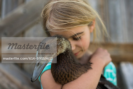 Girl with eyes closed hugging farm duck