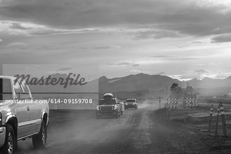 Pick-up and cars on dusty dirt track at dusk, B&W, Browning, Montana, USA