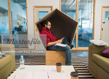Creative businessman using smart phone in office cubby