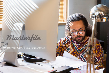 Focused creative businessman reading paperwork at computer in office