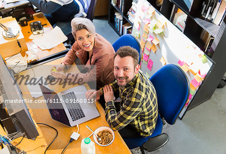 Portrait smiling, confident creative business people eating cereal, working at laptop in office