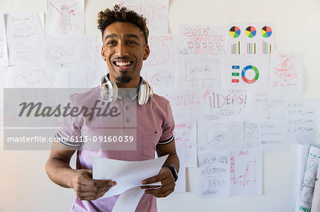 Portrait smiling, confident creative businessman hanging paperwork on office wall