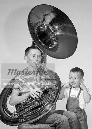 1950s TEEN BOY IN STRIPE SHIRT JEANS PLAYING TUBA SMALLER BROTHER IN BIB OVERALLS SMILING INDEX FINGERS STUCK IN BOTH EARS