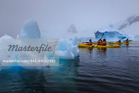 Expedition tourists kayaking in snowy weather, with blue icebergs, Chilean Gonzalez Videla Station, Waterboat Point, Antarctica, Polar Regions Expedition tourists kayaking in snowy weather, with blue icebergs, Chilean Gonzalez Videla Station, Waterboat Point, Antarctica, Polar Regions