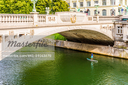 A boy paddle-boarding under Dragon Bridge, Ljubljana, Slovenia, Europe