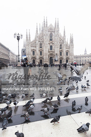 A person feeds pigeons in Piazza Duomo (Cathedral Square), Milan, Lombardy, Northern Italy, Italy, Europe