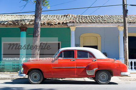 Red vintage American car parked on street next to colourful buildings in Vinales, Cuba, West Indies, Caribbean, Central America