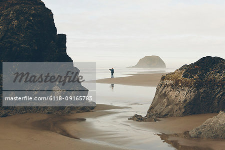 Man taking photos on beach at low tide, Arcadia Beach State Park, Oregon