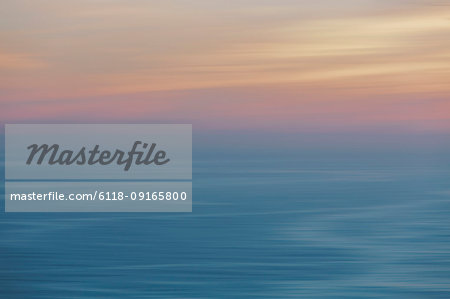 View out to sea over the ocean at dusk,  the sunset light on the horizon and calm undulating sea surface. Abstract coloured light effect.