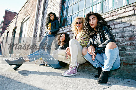 Four young women with curly hair sitting side by side on steps outside a building.