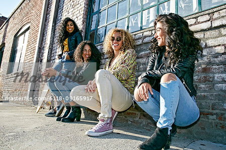 Four young women with curly hair sitting side by side on steps outside a building.