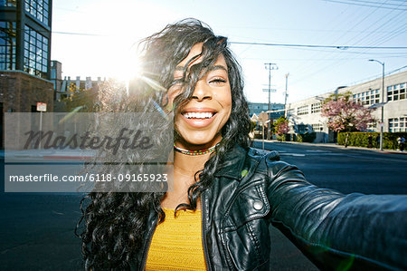 Portrait of young smiling woman with long curly black hair standing on street, looking at camera.