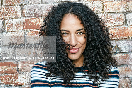 Portrait of young smiling woman with long curly black hair, looking at camera.