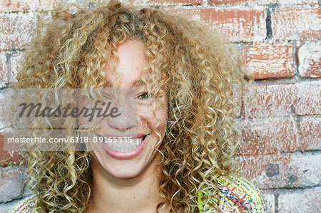 Portrait of young smiling woman with long curly blond hair, looking at camera.