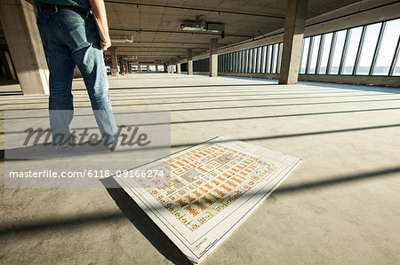 Businessman standing in the middle of an expanse of raw space, and architectural plans on the floor beside him.