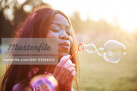 Young woman covered in coloured chalk powder blowing bubbles at Holi Festival