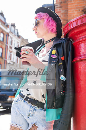 Young woman with pink hair and quirky style leaning against red mailbox, London, UK