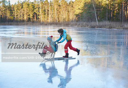 Boy pushing his brother on sleigh across frozen lake