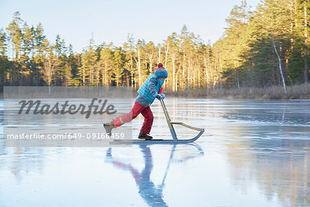 Boy skating on sleigh across frozen lake