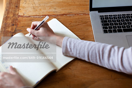 Woman writing notes into notepad from laptop