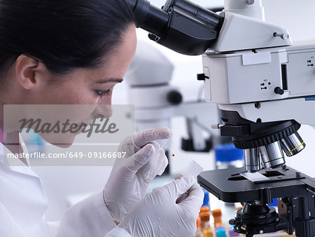 Scientist viewing human sample on glass slide under microscope