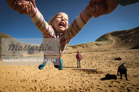 Parent holding daughter's hands, spinning her around, young son in background, low angle view, Lahinch, Clare, Ireland