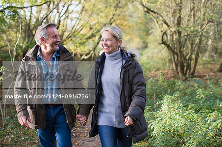 Happy, affectionate mature couple holding hands and walking in autumn park