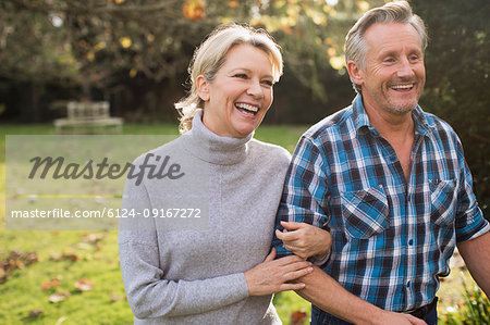 Happy, carefree mature couple walking arm in arm in sunny autumn park