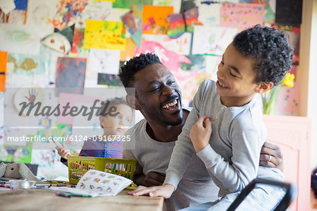 Playful father and son laughing, coloring at dining table