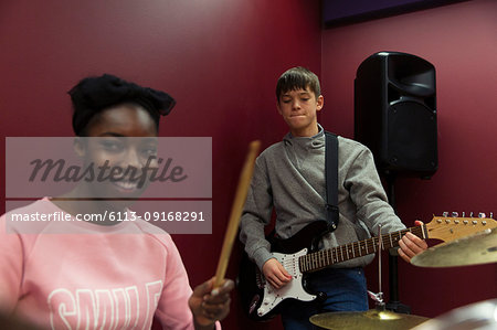 Smiling teenage musicians recording music, singing and playing electric guitar  in sound booth