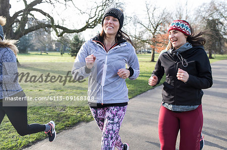 Smiling female runners running in sunny park