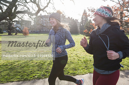 Smiling female runners running in sunny park