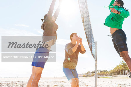 Men playing beach volleyball on sunny beach