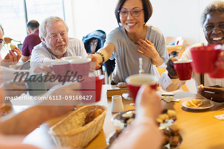 Happy senior friends enjoying afternoon tea, toasting mugs in community center