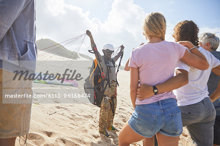 Students watching male paragliding instructor with equipment on sunny beach