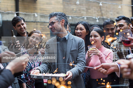Friends with sparklers celebrating with man holding birthday cake