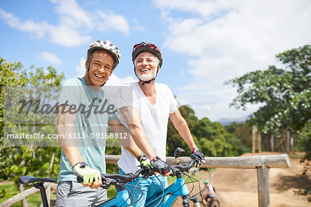 Portrait confident father and son mountain biking on sunny trail
