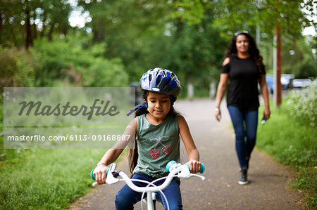 Mother watching daughter bike riding on path