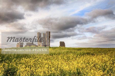 Old ancient ruined church set in a yellow crop landscape with beautiful clouds and sunset sunlight