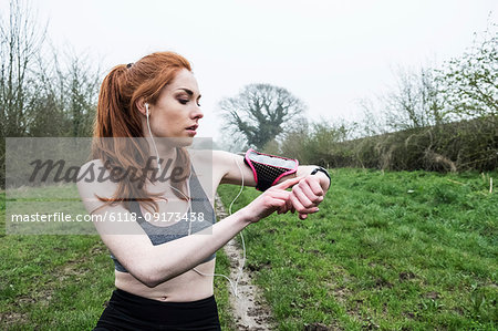 Young woman with long red hair wearing sports kit, exercising outdoors, checking her watch.