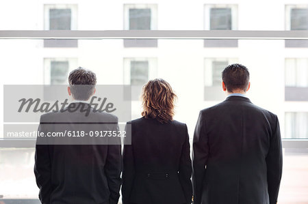 Rear view of group of three business people looking out the window of a conference centre lobby.