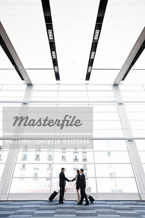 Three business people meeting in front of a large window in a convention centre lobby.