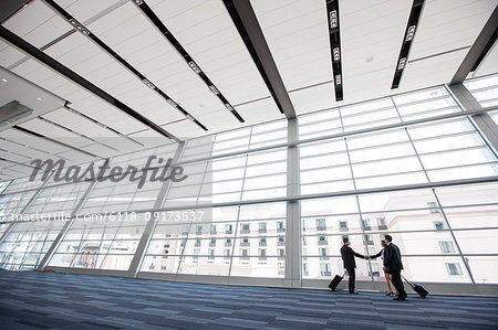 Three business people meeting in front of a large window in a convention centre lobby.