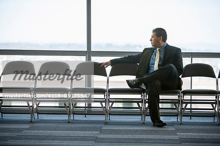 Hispanic businessman sitting in a row of chairs against a window in a conference centre lobby.