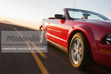 A low angle view of a convertible sports car moving on a highway late in the day.